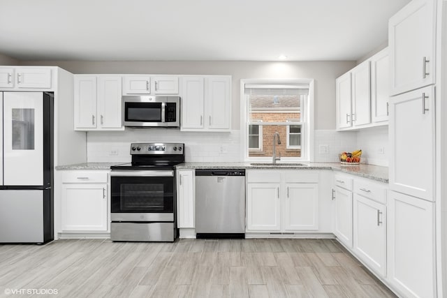 kitchen featuring sink, light stone counters, light hardwood / wood-style floors, white cabinets, and appliances with stainless steel finishes