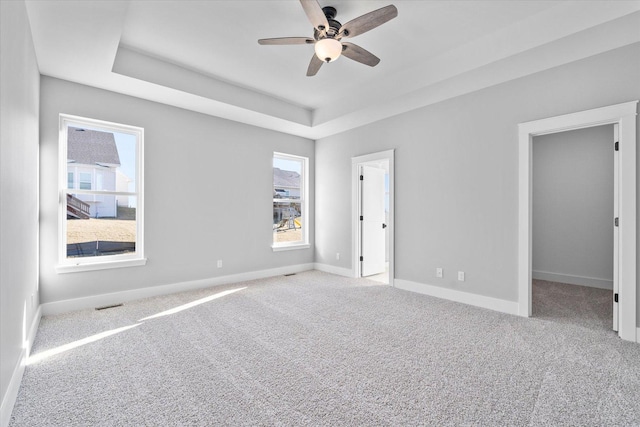 unfurnished room featuring light carpet, ceiling fan, and a tray ceiling