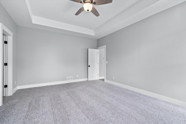 unfurnished room with a raised ceiling, carpet, and ceiling fan