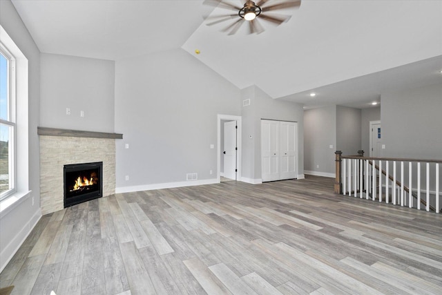 unfurnished living room with ceiling fan, high vaulted ceiling, a fireplace, and light hardwood / wood-style flooring