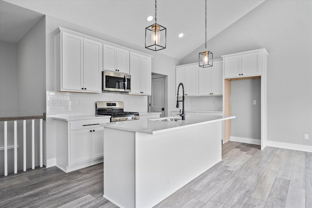 kitchen featuring sink, appliances with stainless steel finishes, white cabinets, a center island with sink, and decorative light fixtures