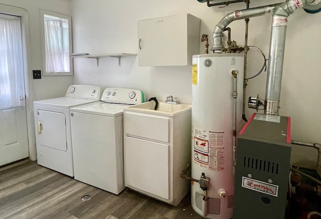 clothes washing area featuring washing machine and clothes dryer, water heater, hardwood / wood-style floors, and cabinets