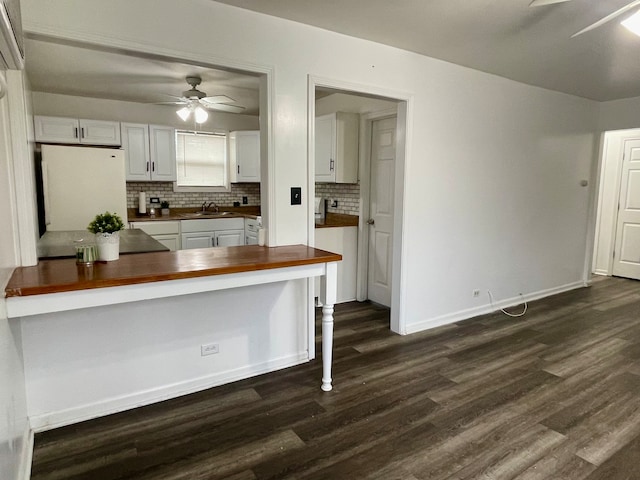 kitchen with kitchen peninsula, dark wood-type flooring, sink, white cabinets, and white fridge