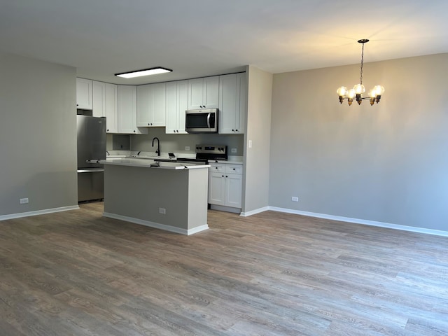 kitchen featuring hardwood / wood-style floors, white cabinetry, hanging light fixtures, and appliances with stainless steel finishes