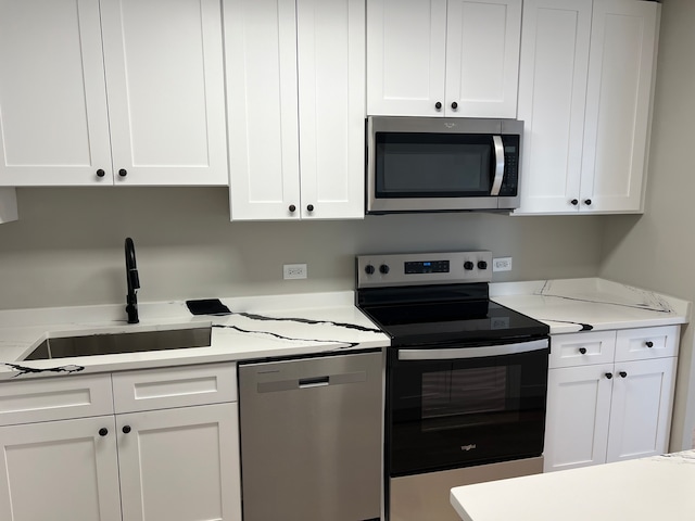 kitchen with white cabinets, stainless steel appliances, light stone counters, and sink