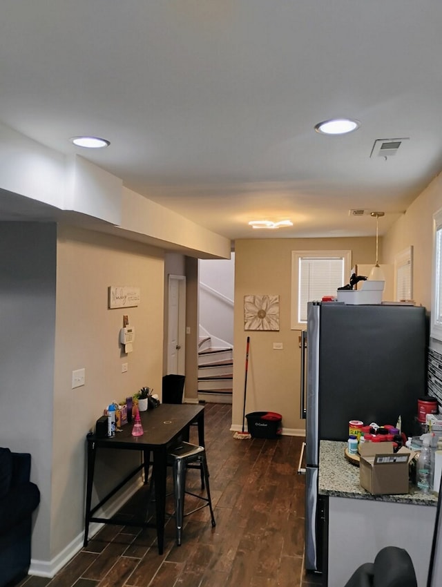 kitchen with dark hardwood / wood-style floors, stainless steel refrigerator, hanging light fixtures, and light stone counters