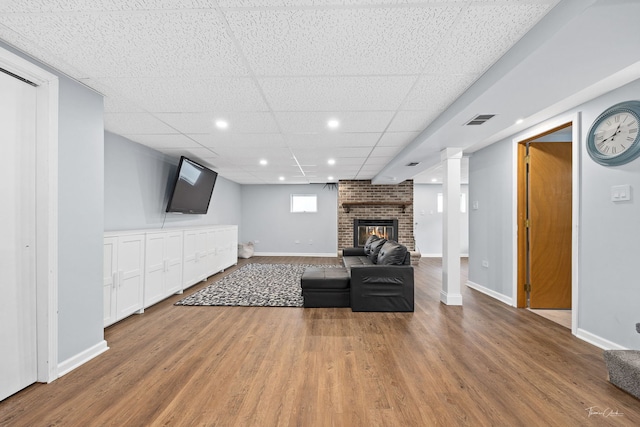 unfurnished living room with hardwood / wood-style flooring, a drop ceiling, and a brick fireplace