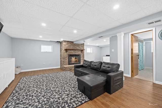 living room featuring a fireplace, wood-type flooring, and a paneled ceiling