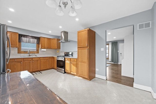 kitchen featuring appliances with stainless steel finishes, tasteful backsplash, wall chimney exhaust hood, sink, and a notable chandelier