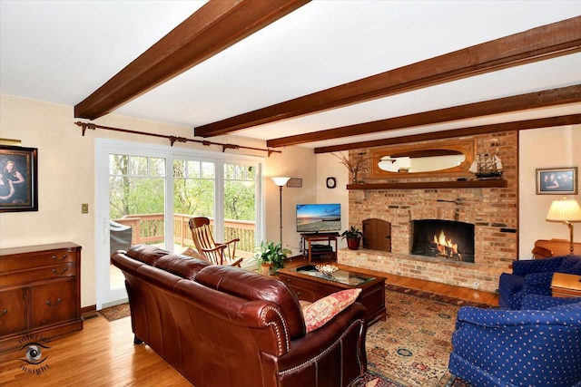 living room featuring beamed ceiling, light hardwood / wood-style floors, and a brick fireplace