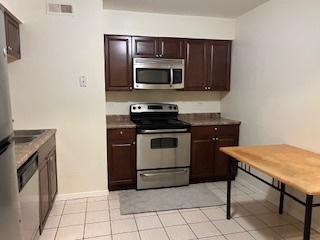 kitchen featuring dark brown cabinetry, light tile patterned floors, and stainless steel appliances