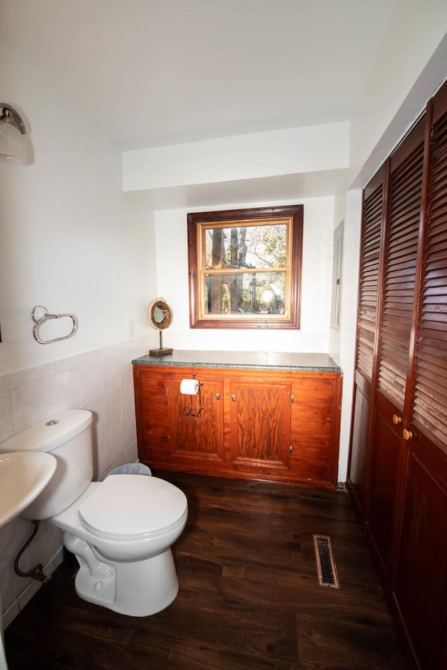 bathroom with toilet, wood-type flooring, and tile walls