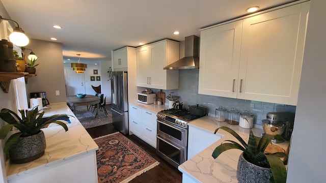 kitchen featuring light stone countertops, stainless steel appliances, white cabinets, and wall chimney range hood