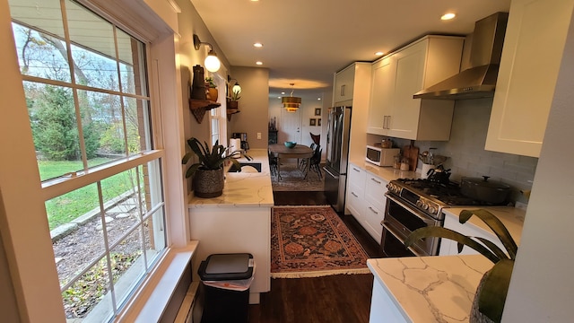 kitchen with white cabinets, wall chimney exhaust hood, light stone countertops, and appliances with stainless steel finishes