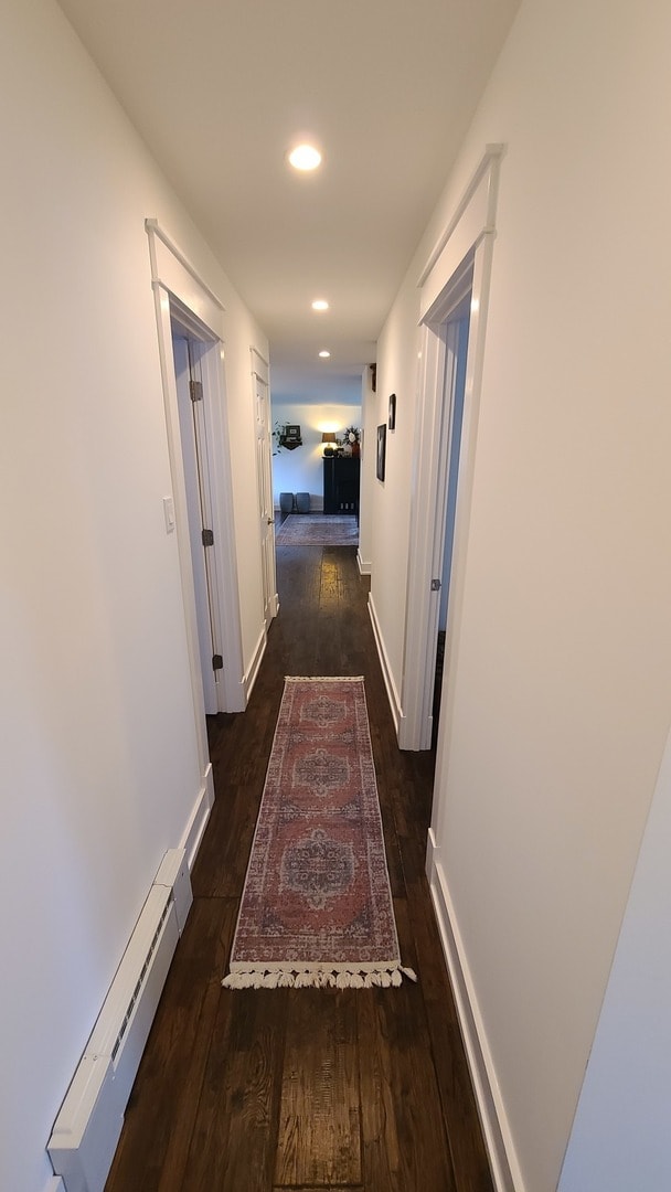 corridor with a baseboard radiator and dark wood-type flooring