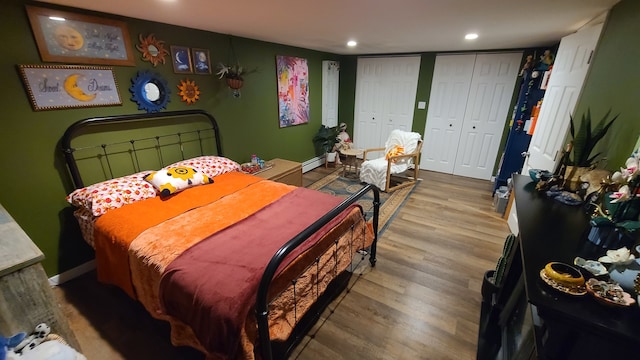 bedroom featuring wood-type flooring, a baseboard radiator, and multiple closets