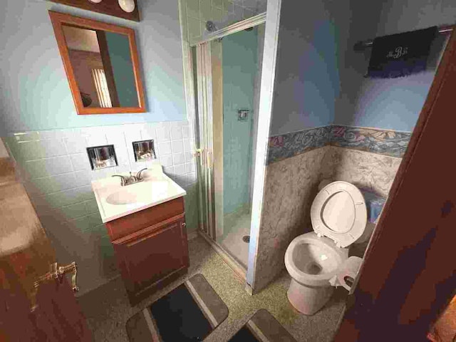 bathroom with vanity, toilet, a shower with door, and tile walls