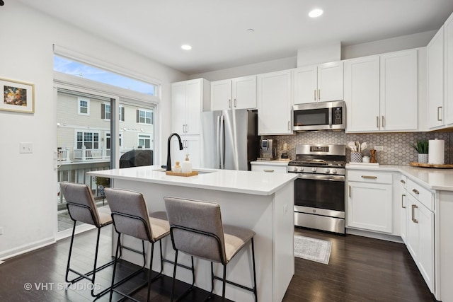 kitchen with appliances with stainless steel finishes, dark hardwood / wood-style flooring, sink, a center island with sink, and white cabinets