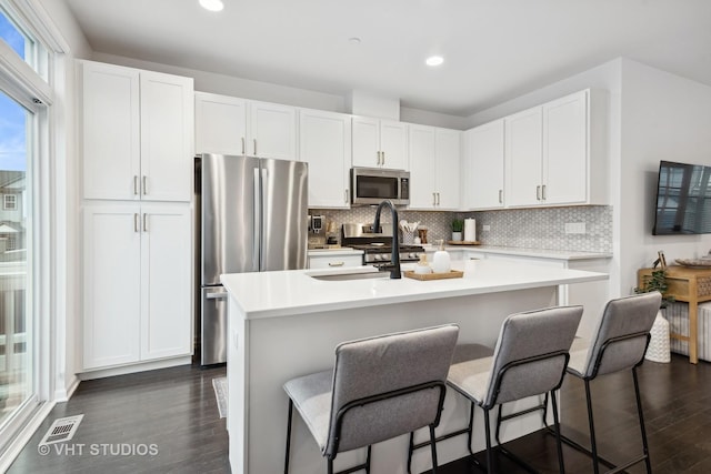 kitchen with a breakfast bar, dark wood-type flooring, white cabinets, an island with sink, and appliances with stainless steel finishes