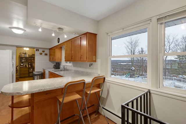 kitchen with sink, tasteful backsplash, kitchen peninsula, white appliances, and a kitchen bar