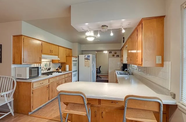 kitchen featuring white appliances, sink, light wood-type flooring, kitchen peninsula, and a breakfast bar area