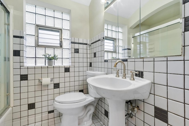 bathroom featuring tile patterned floors, a healthy amount of sunlight, a shower with shower door, and tile walls