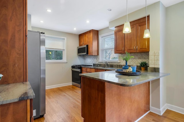 kitchen with appliances with stainless steel finishes, pendant lighting, light hardwood / wood-style flooring, and a healthy amount of sunlight