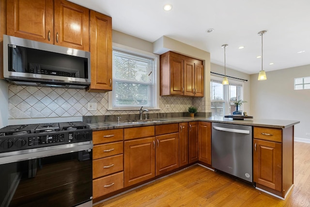 kitchen with backsplash, sink, light wood-type flooring, appliances with stainless steel finishes, and decorative light fixtures