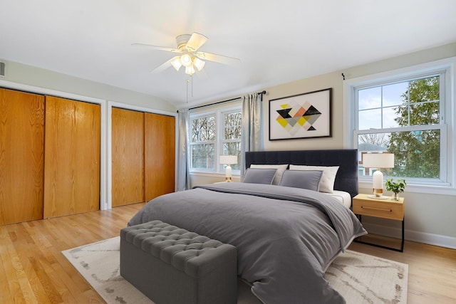 bedroom featuring light wood-type flooring, two closets, multiple windows, and ceiling fan