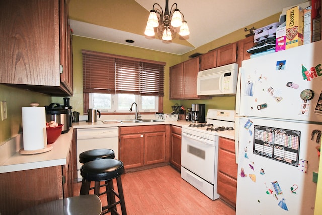 kitchen featuring white appliances, sink, hanging light fixtures, a notable chandelier, and light hardwood / wood-style floors