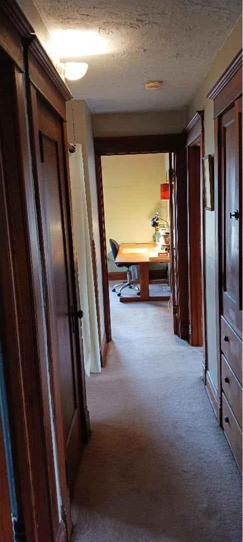 corridor featuring a textured ceiling and light carpet