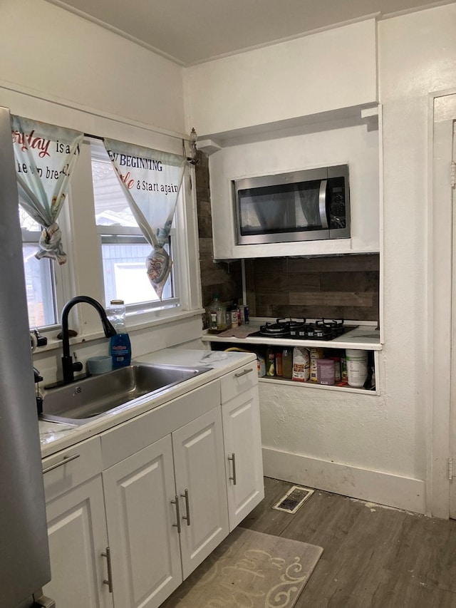 kitchen featuring white gas stovetop, dark wood-type flooring, sink, white cabinets, and stainless steel microwave