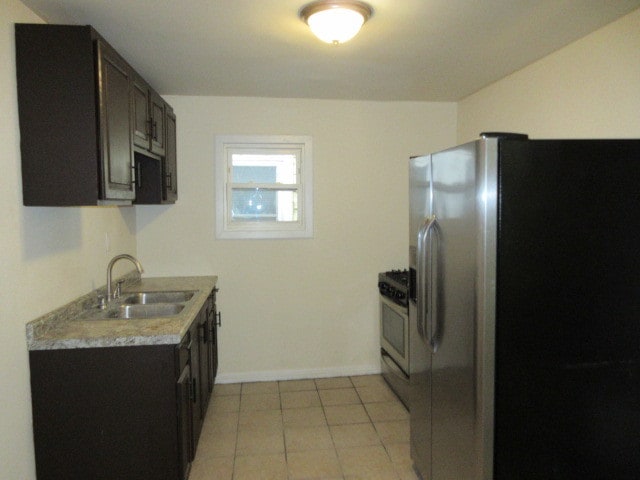 kitchen featuring stainless steel fridge, dark brown cabinetry, white range with gas cooktop, sink, and light tile patterned floors