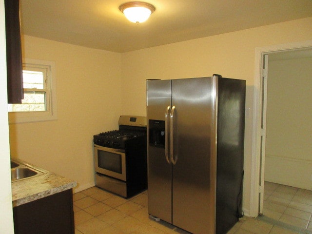 kitchen with stainless steel fridge with ice dispenser, sink, gas range oven, and light tile patterned flooring