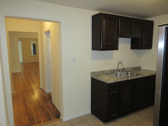 kitchen with stainless steel refrigerator, light stone countertops, sink, and light wood-type flooring