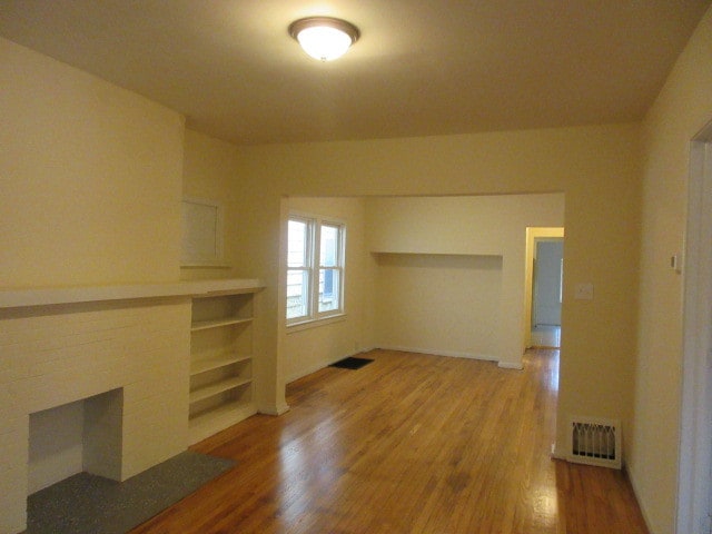 spare room featuring wood-type flooring and a brick fireplace