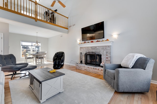 living room with ceiling fan, a fireplace, a towering ceiling, and light hardwood / wood-style floors