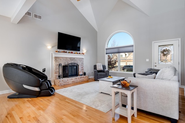 living room with light hardwood / wood-style flooring, high vaulted ceiling, beamed ceiling, and a brick fireplace