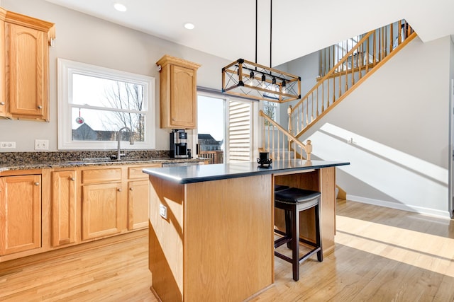 kitchen with light brown cabinetry, a kitchen island, decorative light fixtures, and light hardwood / wood-style flooring