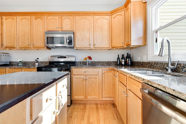 kitchen featuring dark stone countertops, sink, light wood-type flooring, and appliances with stainless steel finishes