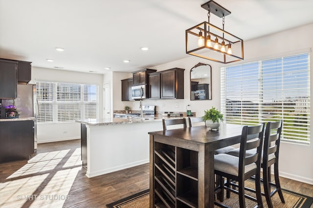 kitchen featuring dark brown cabinetry, dark hardwood / wood-style floors, an island with sink, pendant lighting, and appliances with stainless steel finishes