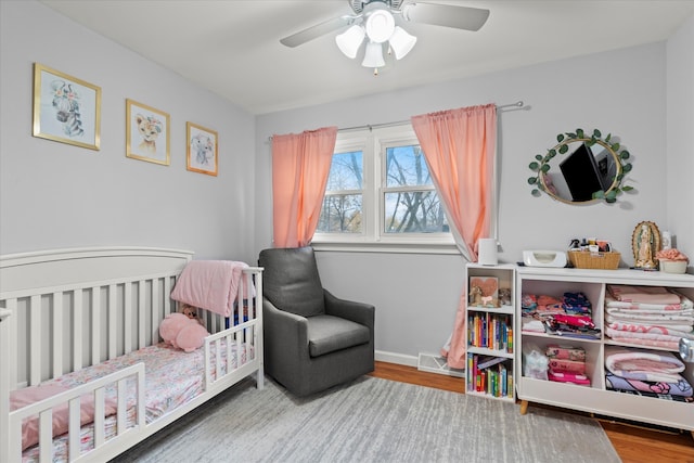 bedroom featuring hardwood / wood-style flooring, ceiling fan, and a crib