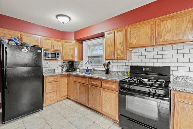 kitchen with light stone countertops, backsplash, sink, and black appliances