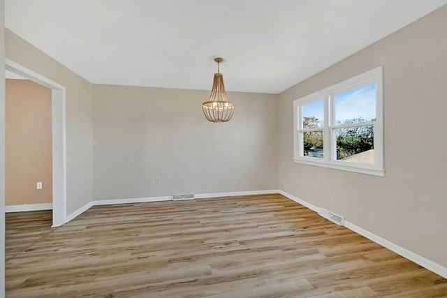 empty room featuring a chandelier and light wood-type flooring