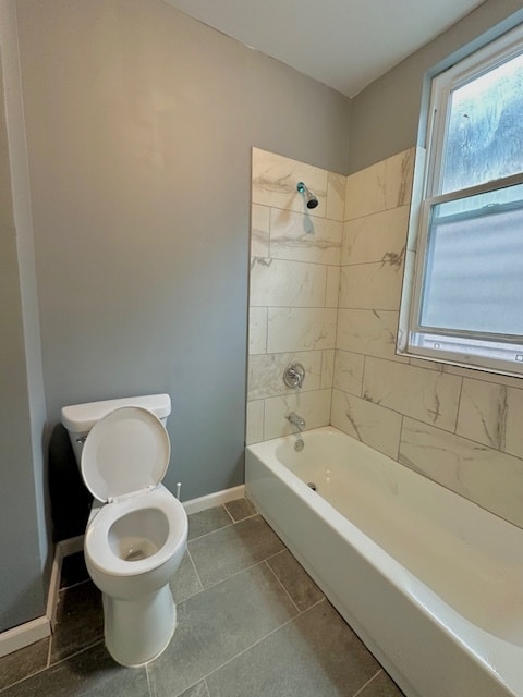 bathroom featuring tile patterned flooring, tiled shower / bath combo, and toilet