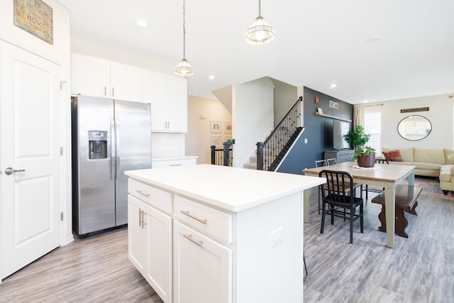 kitchen featuring white cabinets, stainless steel fridge, light hardwood / wood-style floors, and hanging light fixtures