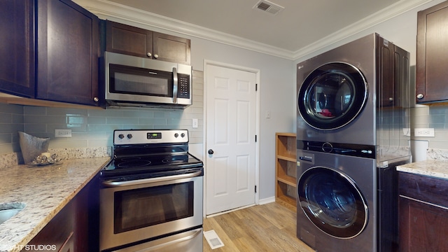 kitchen with ornamental molding, appliances with stainless steel finishes, stacked washer / drying machine, light hardwood / wood-style floors, and light stone counters