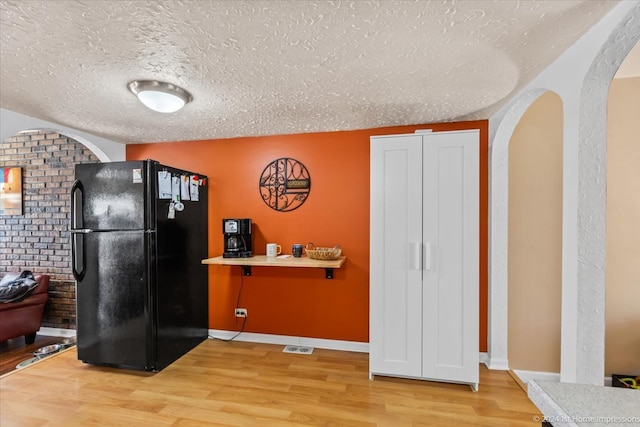 kitchen featuring black fridge, brick wall, a textured ceiling, and hardwood / wood-style flooring