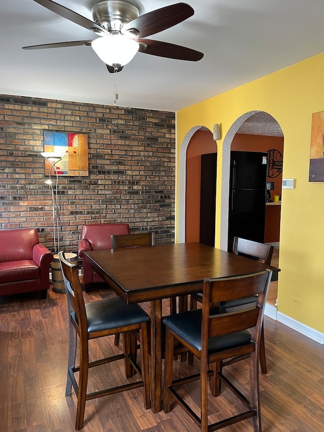 dining room featuring dark hardwood / wood-style floors, ceiling fan, and brick wall