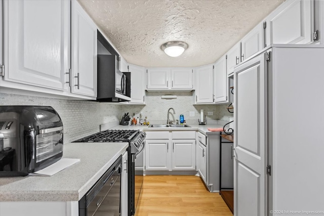 kitchen with white cabinets, black gas range oven, light hardwood / wood-style floors, and sink